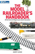 Open book titled "Comprehensive Guide to Model Railroading" with detailed diagrams and illustrations on model train layouts.
